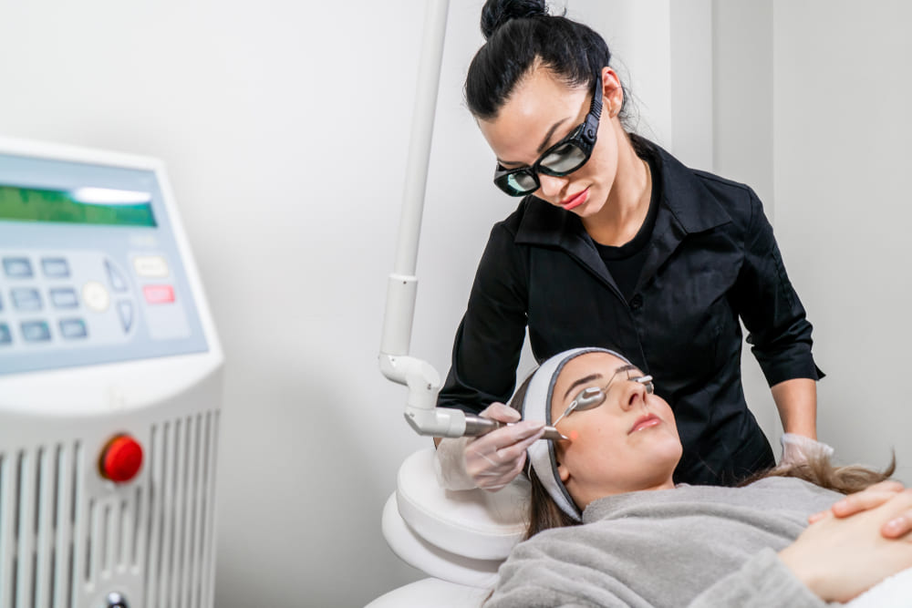 Beauty laser technician performing a cosmetic skin resurfacing session on a female patient