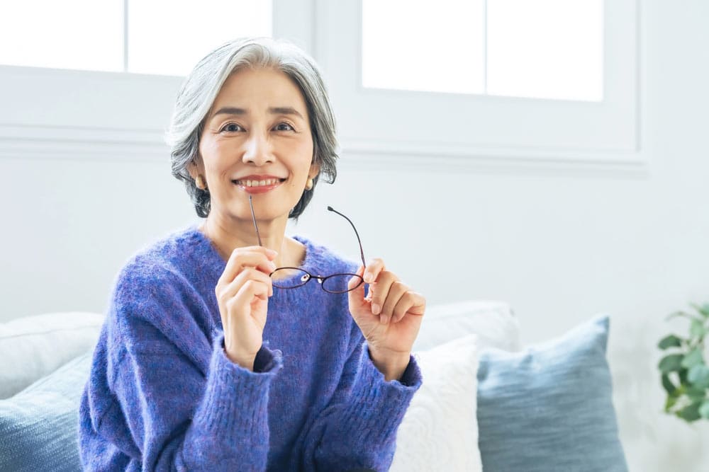 Senior Asian woman taking off her glasses in the living room