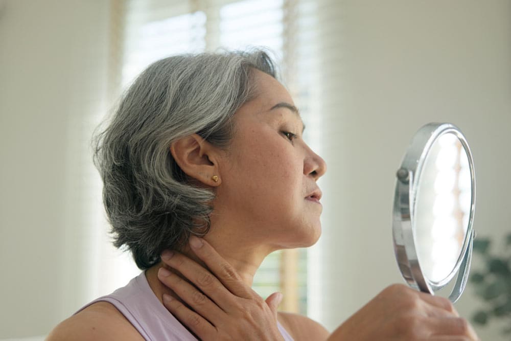 old woman look at mirror dry skin face hand touch neck cheek stress sad at home