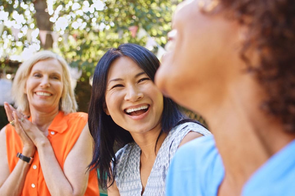 Close Up Of Smiling Mature Female Friends Socializing In Backyard Together