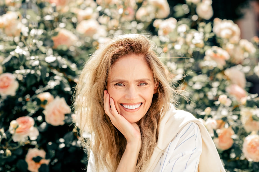 Beautiful mature woman smiling outdoors amidst a garden of blooming flowers during a bright and sunny day
